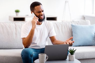 Hoş olmayan bir çağrı. Telefonda konuşan sinirli siyah adam dizüstü bilgisayarla veya evdeki koltukta oturan internet bağlantısıyla ilgili bir sorun yaşıyor. Memnun Olmayan Müşteri Yardım Hattı Konseptine Çağırıyor