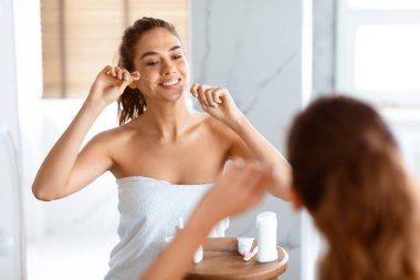 Diş sigortası. Genç bayan diş ipi ile diş ipi temizleme modern tuvalette dikiliyor, aynadaki yansımaya bakıyor. Sabah Ağız Temizliği Rutini. Seçici Odaklanma