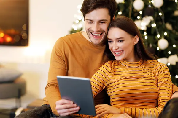 İnsanlar ve Teknoloji. Oturma odasındaki koltukta oturmuş dijital tablet kullanan ve gülümseyen güzel bir çiftin portresi. Mutlu Aile Sörfü İnternet Seçme Hediyesi, İnternette Film İzleme