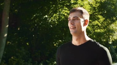 Genç bir adam yaz boyunca verimli bir parkta enerjik bir şekilde koşar, aktif ve sağlıklı bir yaşam tarzını somutlaştırır. Enerjik yeşillik onu çevreledi. Formunu koruyor..