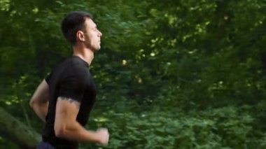 Bir adam yaz günü yemyeşil bir parkta dışarıda koşuyor. Atletik bir duruş sergiliyor ve spor yaparken sağlıklı bir yaşam sürüyor..