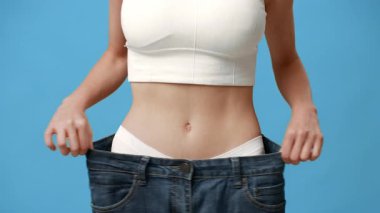 Genç bir kadın gururla büyük beden bir kot pantolon tutuyor ve kilo verme başarısını gösteriyor..