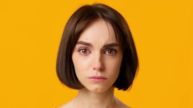 Genç bir esmer kadın hüzünlü bir ifadeyle ayakta duruyor. Gözlerinde yaşlar, belirgin özelliklerini gösteriyor. Parlak sarı arka plan duygularını ön plana çıkarıyor, bir anlık içgözlem anı yakalıyor..