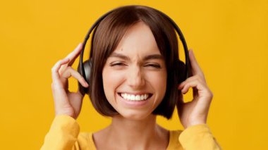 Genç bir esmer kadın kulaklık takıp, müziği emerek ışıl ışıl gülümsüyor. Parlak sarı arka plan, onun neşeli ifadesini yansıtan ana enerji katıyor..