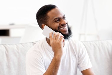 Cep telefonuyla konuşan Afrikalı adam laptopta çalışıyor. Kapalı koltukta oturuyor. Mutlu Black Freelancer Guy telefonda konuşuyor. Serbest Yaşam Tarzı ve Uzak İletişim Konsepti