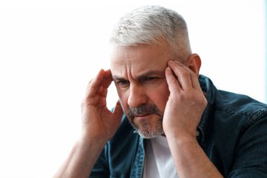 Evde migren ağrısı çeken, şakaklarına dokunan, kopyalama alanı olan olgun, kır saçlı bir adamın yakın çekimi. Yaşlılar için migren, baş ağrısı, stres, gerginlik sorunu