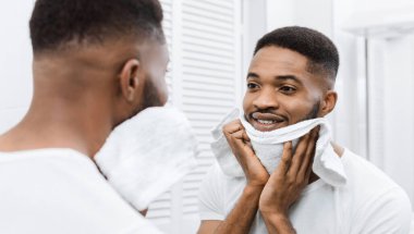 Afro adam tıraş tan sonra yüzünü kurutuyor, banyoda aynaya bakıyor. Metroseksüel sabah rutin kavramı