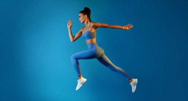 Mavi Stüdyo 'nun arka planında, Havada Atlayan Kararlı Genç Sporcu Kadın' ın yan görünüşü. Havada Koşan Ciddi Fitness Kadınları. Panorama, Tam Uzunluk