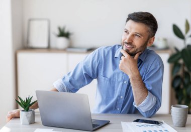 Ofiste çalışırken bir şey düşünen düşünceli erkek girişimci, iş çözümünü buldu, mutlu bir yüz ifadesiyle başka yere baktı.