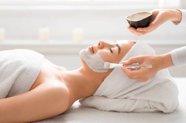 Kadın yüzüne çamur maskesi takan spa terapistinin yan görünüşü