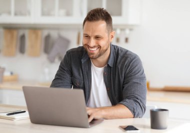 Evde rahat bir iş. Genç, mutlu, bağımsız bir müteahhit. Dizüstü bilgisayarda çalışıyor, gülümsüyor, uzaktan işten zevk alıyor.