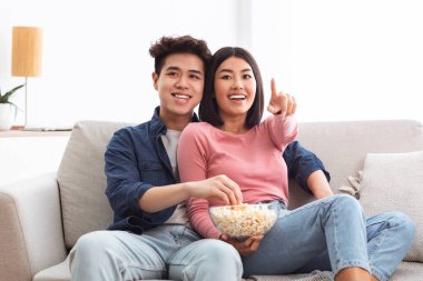 TV 'de komedi filmi seyreden, patlamış mısır yiyen hafta sonunu birlikte evde koltukta oturarak geçiren neşeli Asyalı çift. Koreli Eşler Oturma Odasında Sinemadan Hoşlanıyor