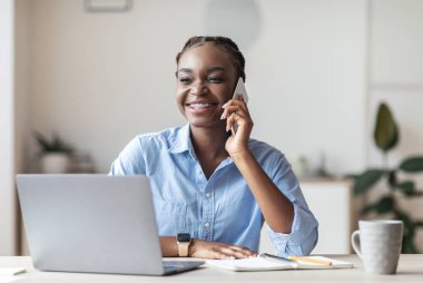 Ofiste cep telefonuyla konuşan genç siyahi bir girişimci müşteriye danışıyor, gülümsüyor ve başka yöne bakıyor.