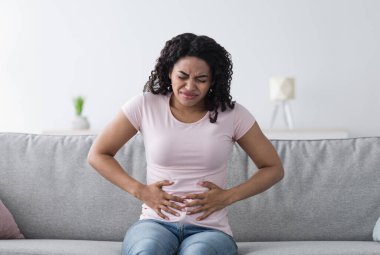 Hastalık, kötü his, mide sorunları, regl, hastalık ve zehirlenme. İç kısımlarında, gri iç kısımlarında, iç kısımlarında karın ağrısından muzdarip binlerce yıllık üzgün Afrikalı Amerikalı kadın.