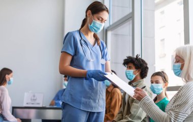 Çeşitli insanlar iğne olmak ya da hastanede Covid-19 enfeksiyonu için test yaptırmak için sırada bekliyorlar. Zatürree, grip ya da koronavirüse karşı aşı için Bilgilendirilmiş Onay belgesi imzalayan kıdemli hasta