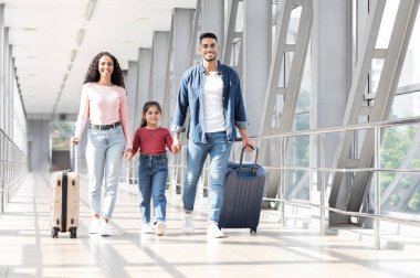 Tatil gezisi. Havaalanı Terminali 'nde bavulla gezen mutlu bir Arap ailesi, küçük kızıyla el ele tutuşan gülümseyen Orta Doğulu ebeveynler,