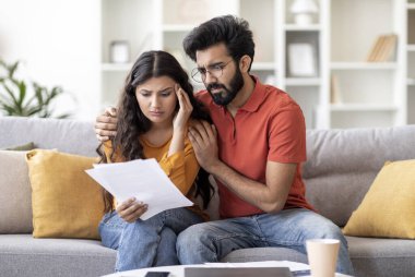 Haberler kötü. Bankadan mektup okuyan üzgün Hintli çift, evdeki koltukta otururken depresyondaki genç Doğu eşlerinin borçları, mali krizleri, kredi talebini reddetmeleri, kapatmaları...