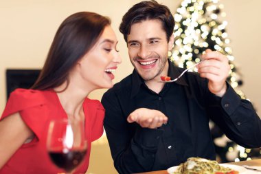 Portrait of affectionate young couple having dinner, smiling guy feeding his girlfriend with pasta. Cute lovers having romantic date, flirting, having fun, celebrating St Valentines Day or holiday