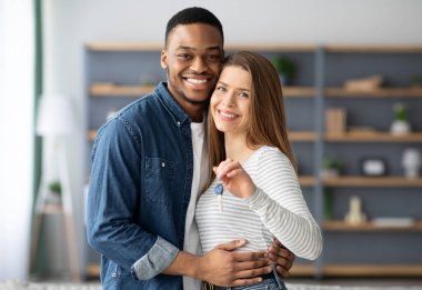 Konut kavramı. Mutlu, genç, ırklar arası eşlerin ev anahtarları ve kucaklayıcı, romantik, çok kültürlü, siyah erkek ve beyaz kadının portresi Yeni Daire 'ye taşınıyor.