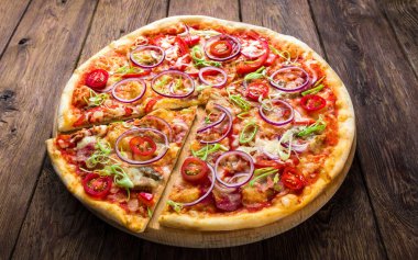 Tahta zemin üzerinde pizza, soğan, pastırma ve kiraz domatesli ince hamur kabuğu, yakın plan.