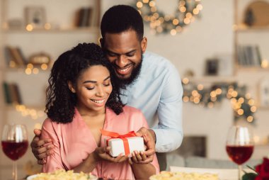 Yakışıklı Afro-Amerikalı genç adam, heyecanlı kız arkadaşına paketlenmiş hediye paketi sunuyor ve ona özel bir sürpriz yapıyor. Sevgili çift Sevgililer Günü 'nü, doğum gününü ya da yıldönümünü kutluyor.