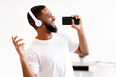 Afrika kökenli Amerikalı bir adam mikrofon gibi şarkı söylüyor. Evde duran kulaklıkla müzik dinlerken eğleniyor. Mobil Karaoke Uygulaması Kavramı