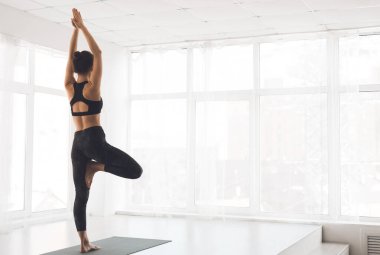 Vrksasana Or Tree Pose. Back view of slim girl standing by window in modern studio, copyspace, full length