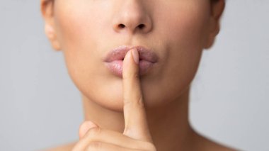 Kadınların sırları. Gri arka planda parmaklarını dudaklarında tutan bir kadın.