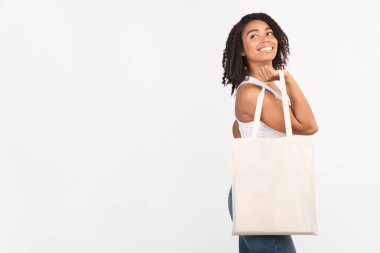 Ekoloji Konsepti. Beyaz pamuklu çantalı siyah kadın beyaz arka planda fotokopi alanına bakıyor.