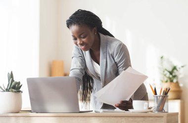 Başarılı bir proje. Gülümseyen Afro İş Kadını Modern Ofiste Evraklar ve Bilgisayarla Çalışıyor, Beleş Alan