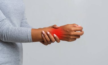 Cropped image of afro woman suffering from rheumatism, massaging her wrist, grey background