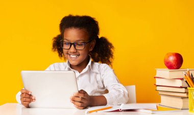 Gülümseyen Afro Öğrenci Kız Tablet Bilgisayar kullanarak Sarı Stüdyo Arkaplanının üzerinde oturuyor. Okul ve Gadget Kavramı.