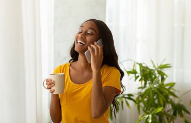 Evde bir fincan aromalı kahveyle cep telefonuyla konuşan çekici siyahi kadın. Çekici Afrikalı Amerikalı kadın cep telefonuyla konuşuyor.