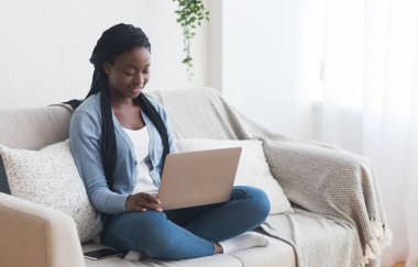 İşe alım kavramı. Afro-Amerikan kadın iş fırsatlarını internette tarıyor, iş arama sitesini evdeki koltukta otururken kullanıyor.