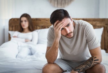 Cinsel işlev bozukluğu. Üzgün koca başını tutuyor, üzgün eş yatak odasında yatıyor.