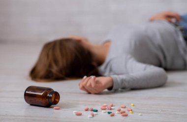 Genç bir kadın aşırı dozda hap alarak intihar ediyor. Yere saçılmış bir şişe tablete odaklan. Depresyon ve aşırı uyuşturucu kullanımı, zihinsel çöküntü veya travma sonrası stres bozukluğu sorunu kavramı