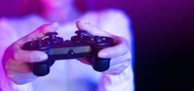 Bir kadın canlı bir mor ışığın önünde elinde bir video oyun kumandası tutarken görülüyor, oyun seansına katılıyor. Kontrolör parlak mor parıltıyla aydınlanır ve çarpıcı bir kontrast yaratır..