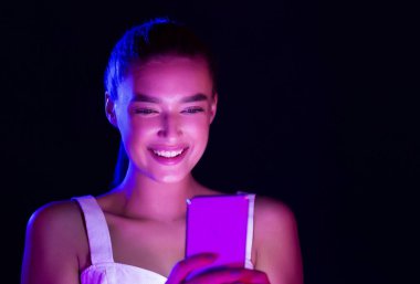 Mutlu kadın telefon kullanarak, stüdyoda neon ışıkları ile aydınlatılmış, kopya alanı