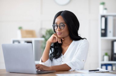 İş yerinde dizüstü bilgisayar kullanan, belge yazan, çevrimiçi iş toplantısına katılan pozitif kadın yönetici. Genç siyahi girişimci Webinar projesine katılıyor.