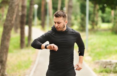 Sabah Rutini Konsepti. Parkland 'da koşan yakışıklı adamın portresi, akıllı saatinde kalp atışlarını kontrol ediyor.