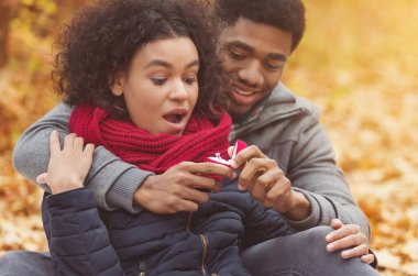 Afro adam kız arkadaşına evlenme teklif ediyor, elinde yüzüklü kırmızı kutu, sonbahar parkında flört ediyor.