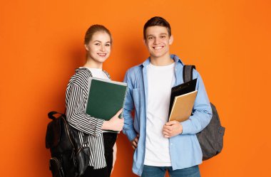 Eğitim konsepti. Sınıf arkadaşları turuncu arka planda egzersiz kitaplarıyla poz veriyorlar.