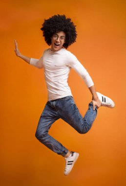 Eğleniyor, hava, turuncu studio arka planda tek ayak üzerinde atlama neşeli gür siyah adam