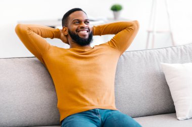 Keyifli siyah adam koltukta oturuyor, el ele tutuşuyor, içeride dinleniyor. Evin rahatlığı ve konforu. Adam koltukta dinleniyor, tembelliğin tadını çıkarıyor. Haftasonu Gevşeme Konsepti