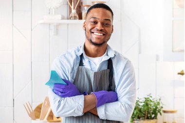Önlüklü genç siyahi adam portresi ve mutfakta kameraya gülümseyen lastik eldivenler. Mutlu Afrikalı Amerikalı adam evini toplamaya, ev işlerini yapmaya, ev işlerini yapmaya hazır.