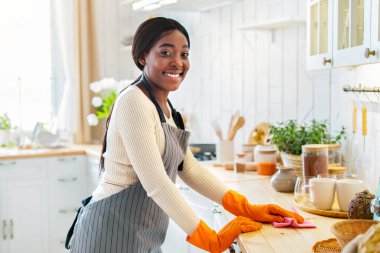Önlüklü genç siyah bayan ve mutfak masasını silen lastik eldivenler, arka planda bulaşık yıkayan erkek arkadaşı, fotokopi alanı. Genç Afrikalı Amerikalı aile birlikte ev işleri yapıyor.