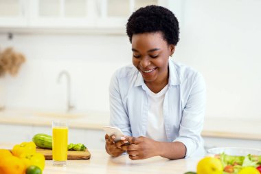 Kilo verme uygulaması. Afro-Amerikalı kadın, evde mutfaktayken zayıflamak için sağlıklı yemek tarifleri kullanıyor. Beslenme Uygulaması ve Kilo Verme Konsepti