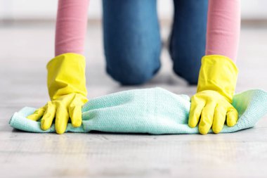 Tanınmayan bir kadın toz beziyle yerleri temizliyor, renkli lastik eldivenler giyiyor, yakın plan. Sıradan kıyafetlerle temizlenmiş bir kadın. Evin zeminini siliyor, evi tek başına temizliyor.