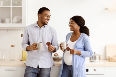 Siyah bir ailenin mutfakta çay içmesini beklemeyi, konuşmayı ve birbirine bakmayı seviyorum. Neşeli Afro-Amerikan hamile kadın ve kocası kupayla kakaonun ve kurabiyelerin tadını çıkarıyorlar.