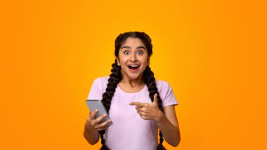 Evet, harika haberlerim var. Heyecanlı Hintli Kadın Portresi Kazananı Kutluyor, Akıllı Telefon Kullanıyor ve Gadget 'ı Gösteriyor, Gülümseyen Genç Bayan Başarılı Oluyor, Cep Telefonu Tutuyor, Sarı Stüdyo Arkaplan
